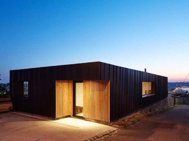 Une maison construite en pleine pente - Une maison en zinc noir posée sur un mur en brique
